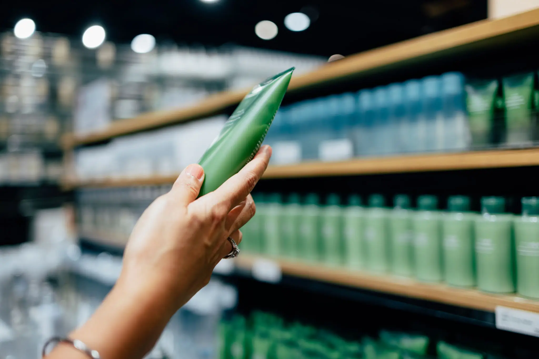 Hand holding a green bottle in a store aisle.
